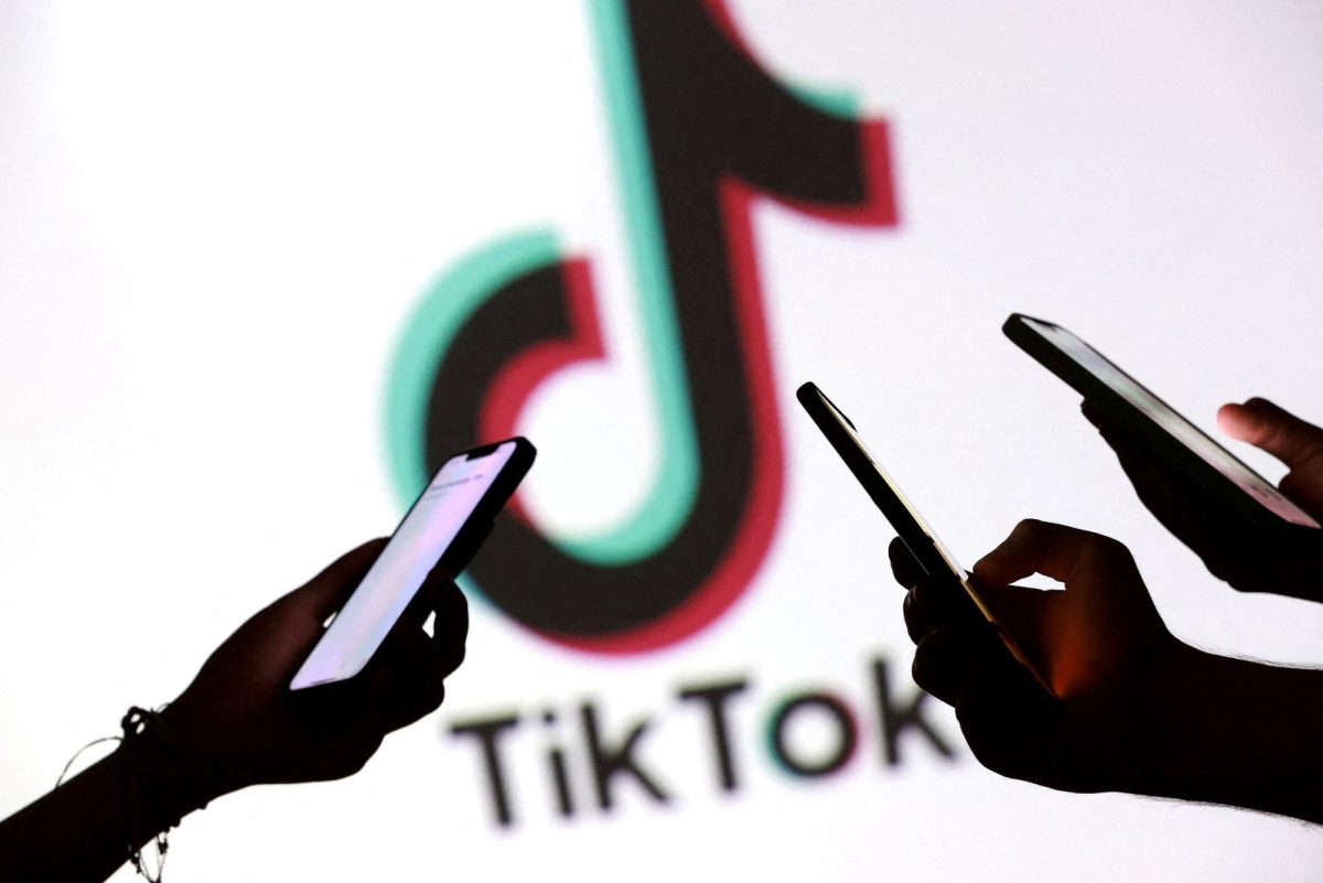 Teenagers pose for a photo while holding smartphones in front of a TikTok logo in this illustration taken September 11, 2025. REUTERS/Dado Ruvic/Illustration